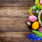 Easter decorations on wooden table, colored eggs and flowers. Top view