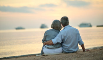Portrait of happy mature couple relaxing on beach at sunset