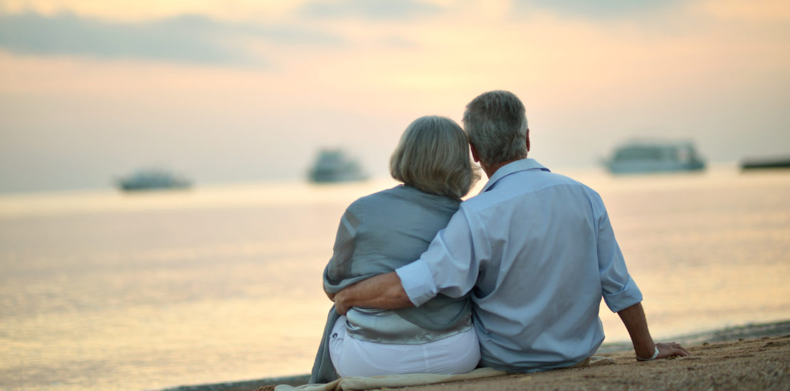 Portrait of happy mature couple relaxing on beach at sunset